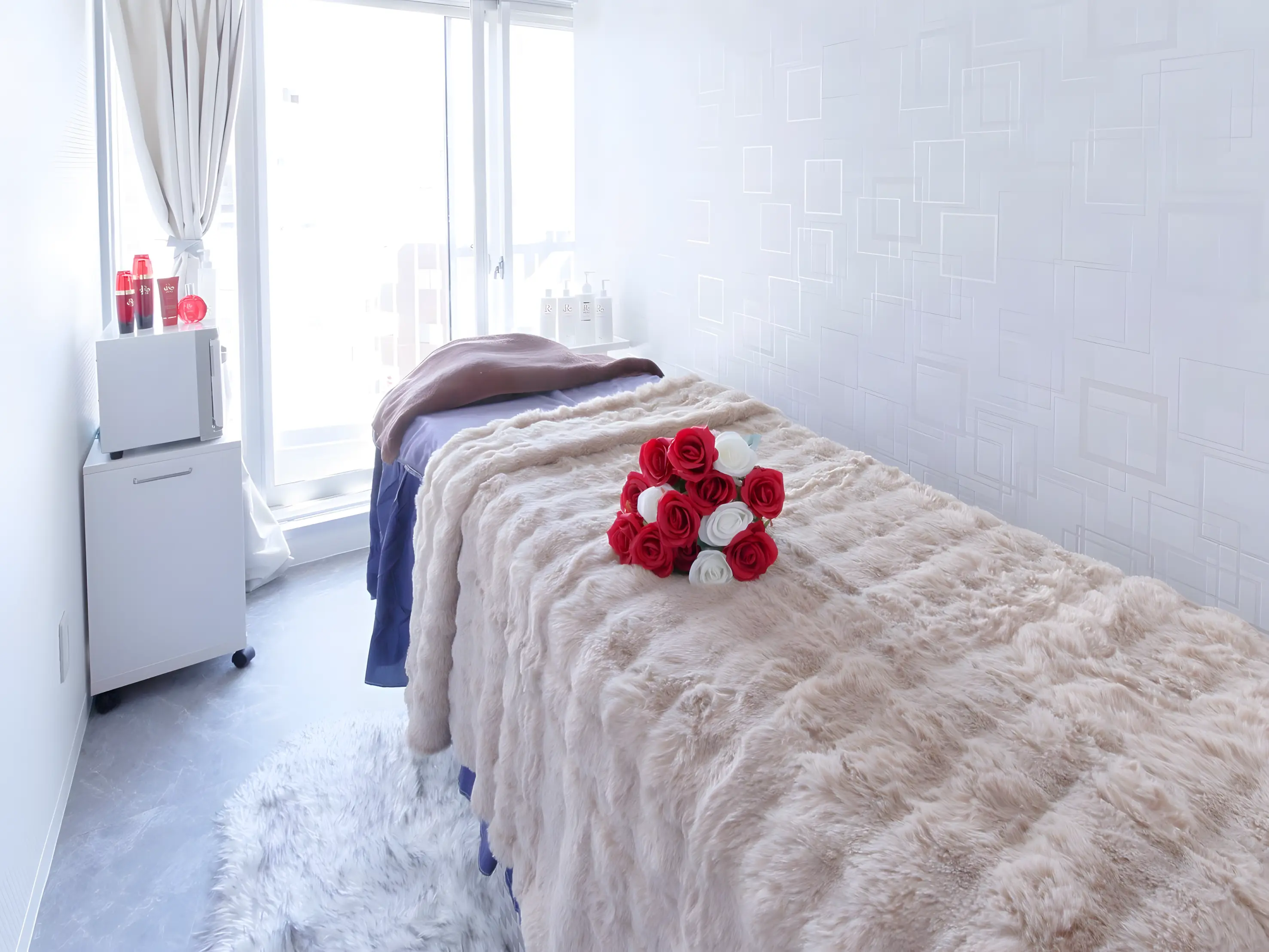 Coco salonの施術室。窓辺のベージュのベッドと、赤と白のバラ